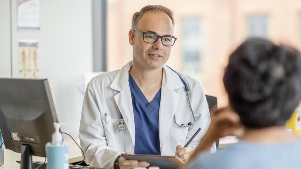 Ein Arzt sitzt am Schreibtisch und spricht mit einer Patientin.