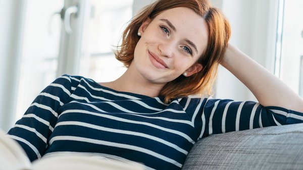 Eine Frau auf einem Sofa schaut lächelnd in die Kamera.