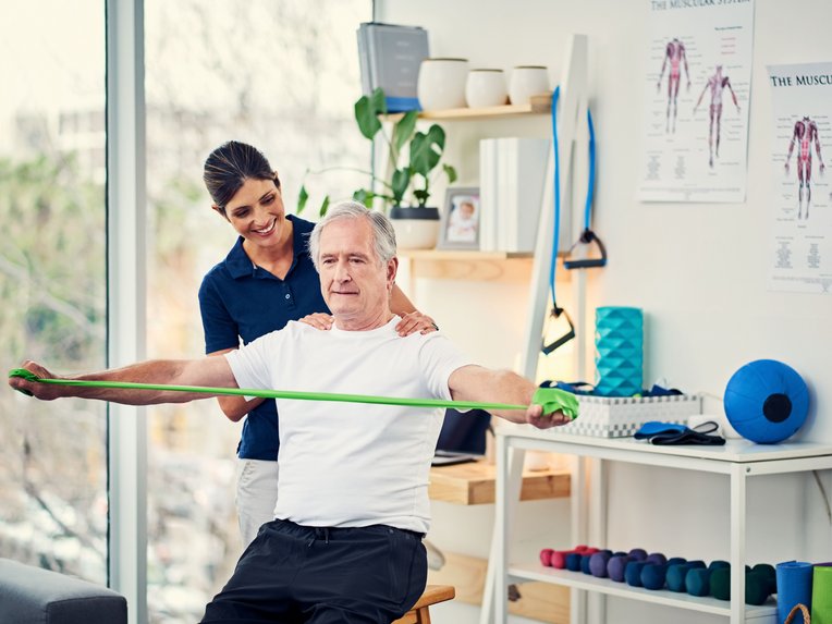 Ein Mann macht Kraft&uuml;bungen, begleitet von einer Physiotherapeutin.
